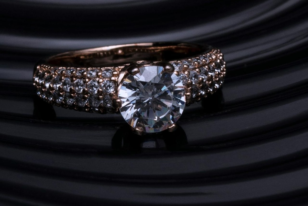 A side stone engagement ring with three rows of pavé diamonds on a dark, striped surface.