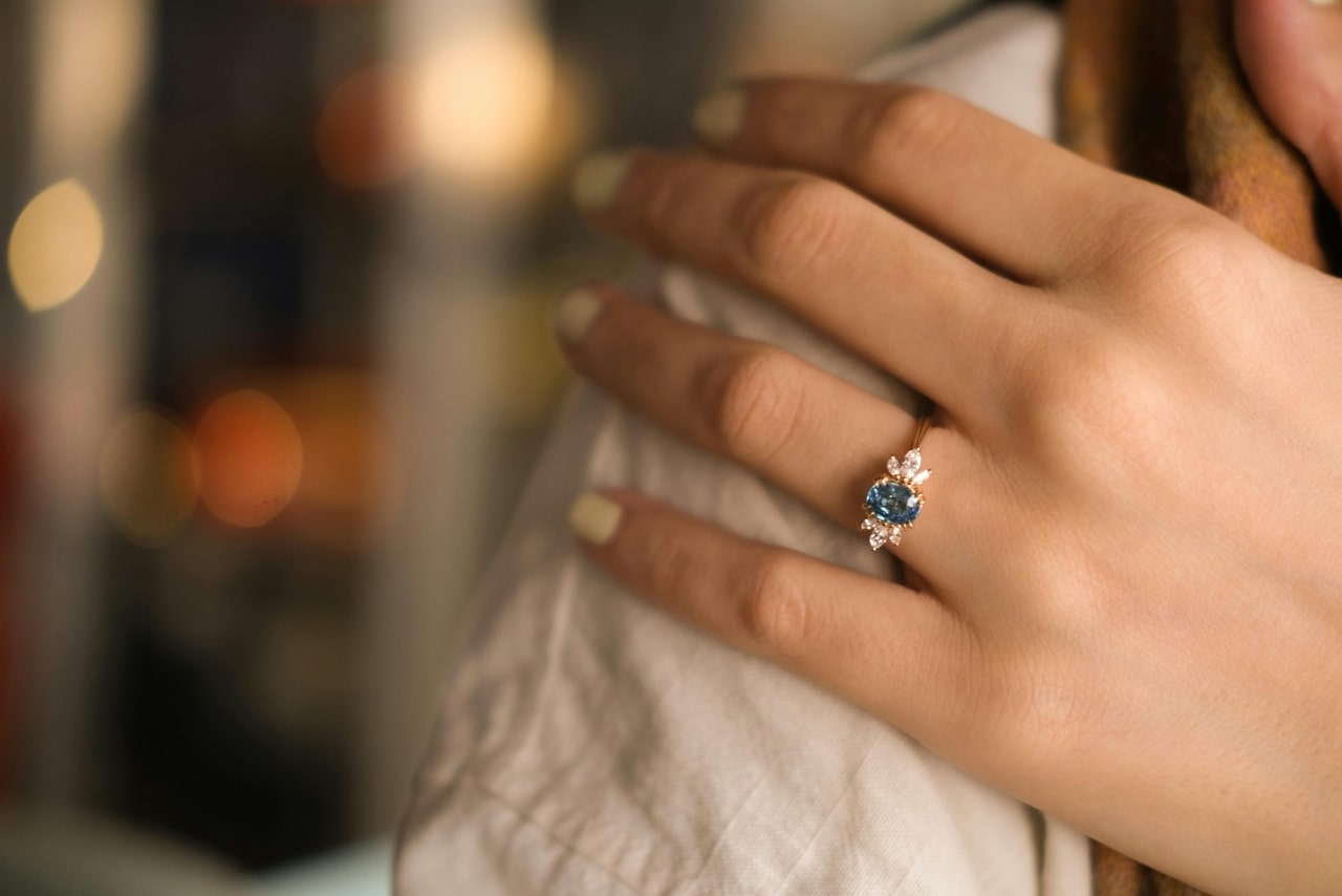 a woman’s hand resting on someone’s shoulder, adorned with a vintage engagement ring